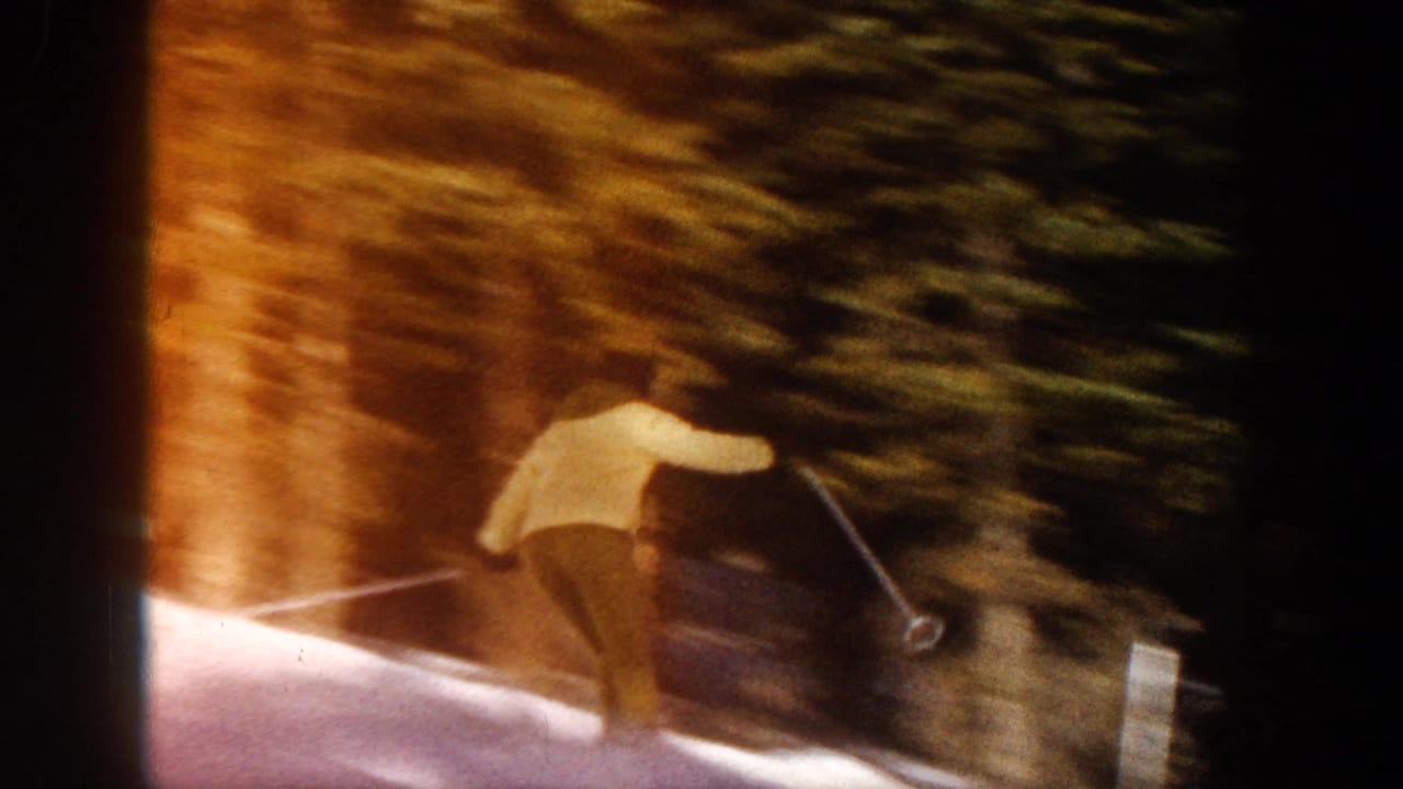 1961 Aspen home-movie frame showing a skier in a light jacket moving downhill near dark evergreen trees.