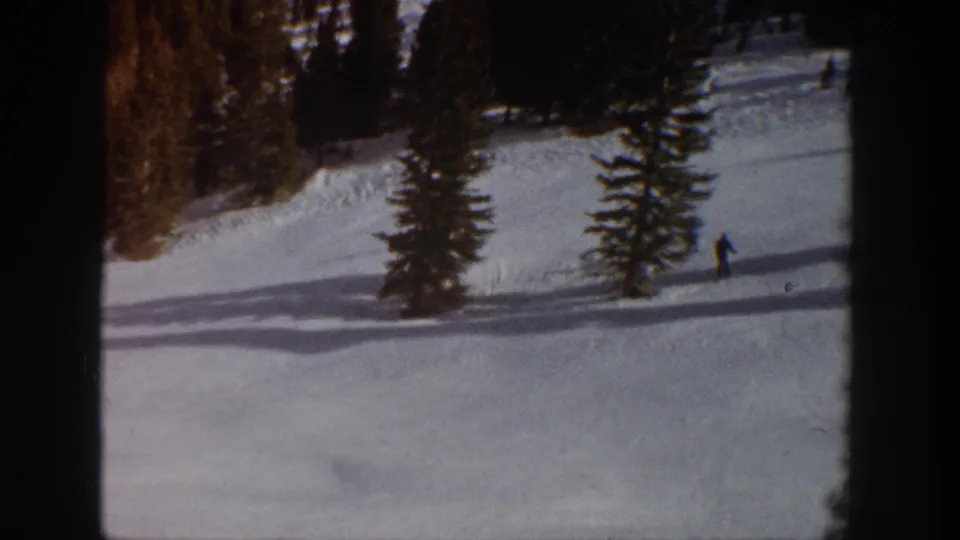 A lone distant skier appears near the right side of the Aspen snowfield, with pine trees, shadow bands, and warm 8mm film texture visible across the frame.