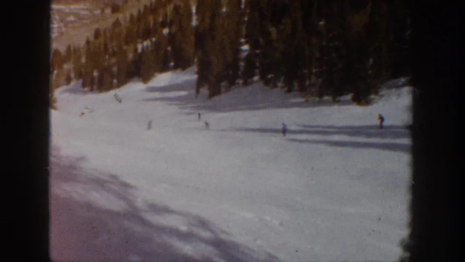 Final 8mm frame shows distant skiers on a broad Aspen snow slope, with evergreen trees and warm film coloration.