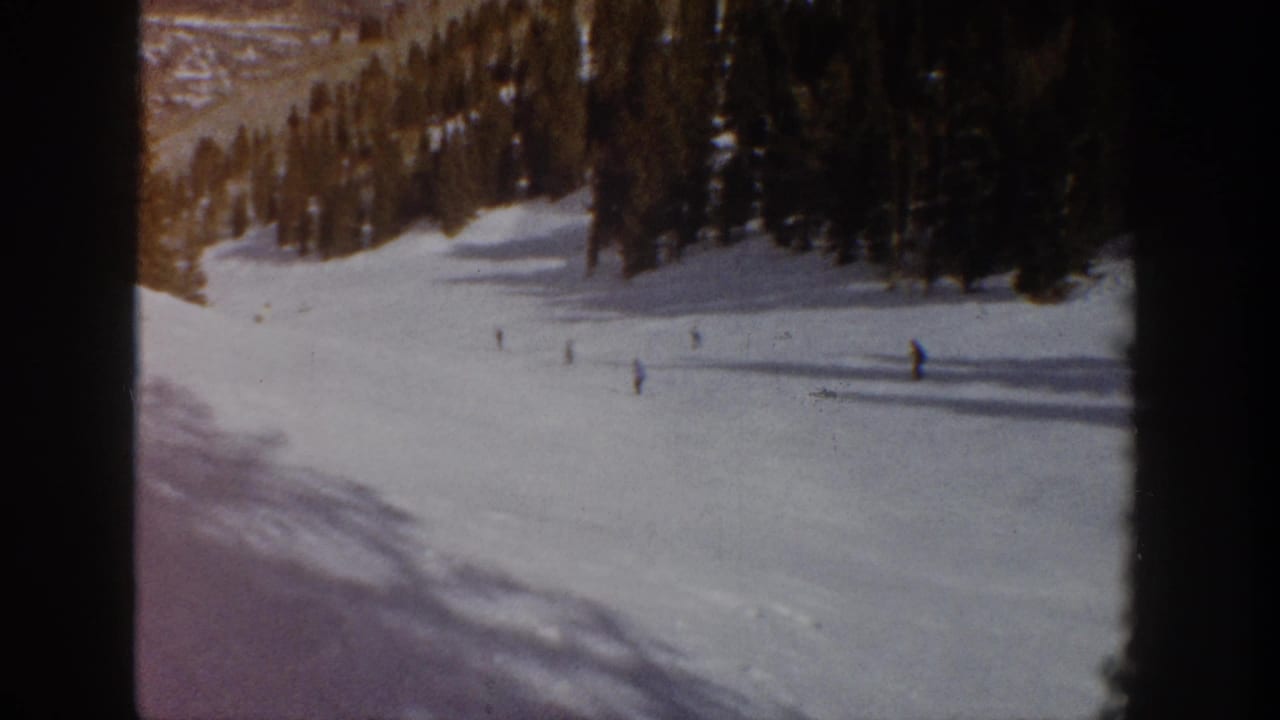1961 Aspen, Colorado 8mm frame showing distant skiers scattered across a broad snow-covered run near dark evergreen trees.