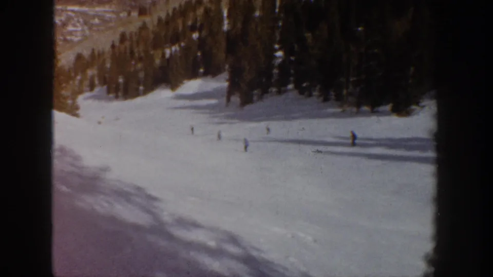 1961 Aspen, Colorado 8mm frame showing distant skiers scattered across a broad snow-covered run near dark evergreen trees.