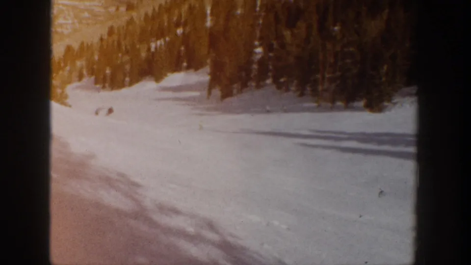 Warm-toned 8mm frame of the Aspen slope in 1961, with distant skiers against snow and a dark evergreen border.