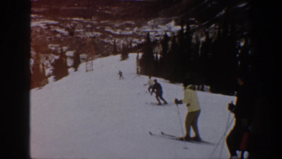 1961 Aspen, Colorado 8mm frame showing skiers on a slope, including nearer figures at right and distant mountain scenery.