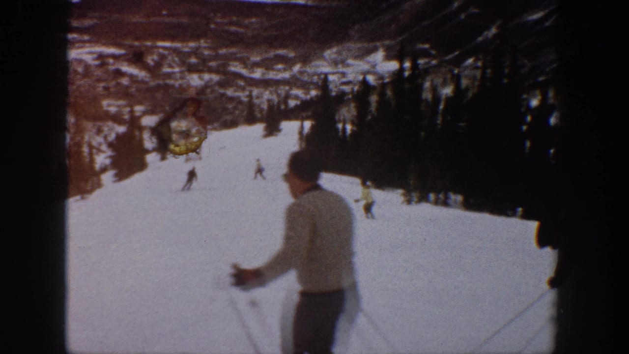1961 Aspen home-movie frame showing skiers on a snowy slope with trees and distant mountain terrain.