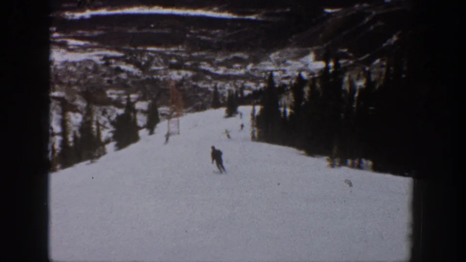 A lone skier moves down a snowy Aspen, Colorado slope in 1961, with trees and distant mountain terrain in soft 8mm color.
