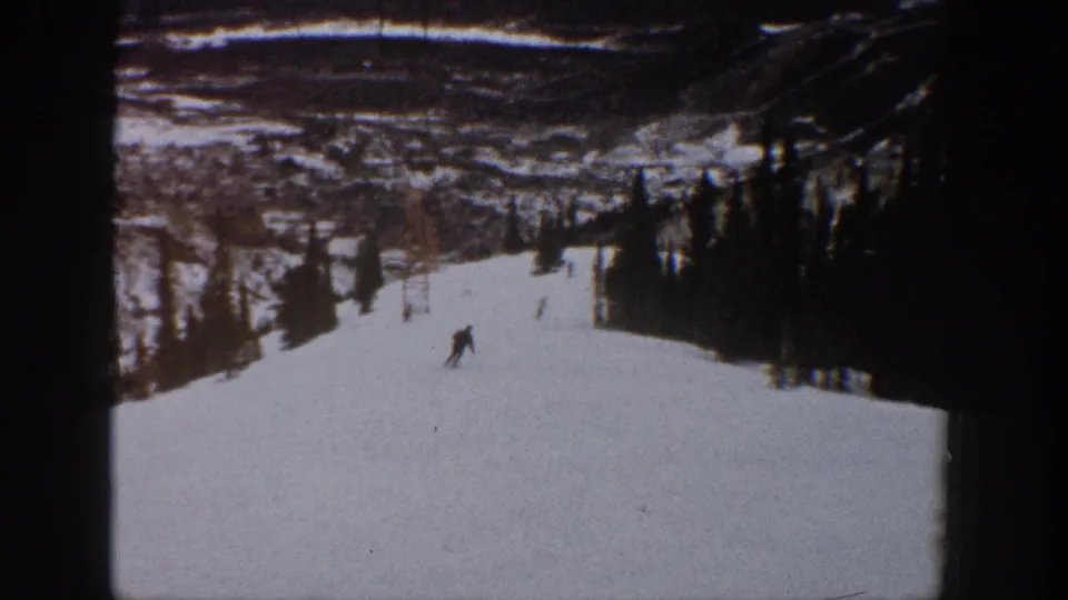 The skier appears farther down the Aspen ski slope, framed by evergreen stands and distant snowy mountain landscape.