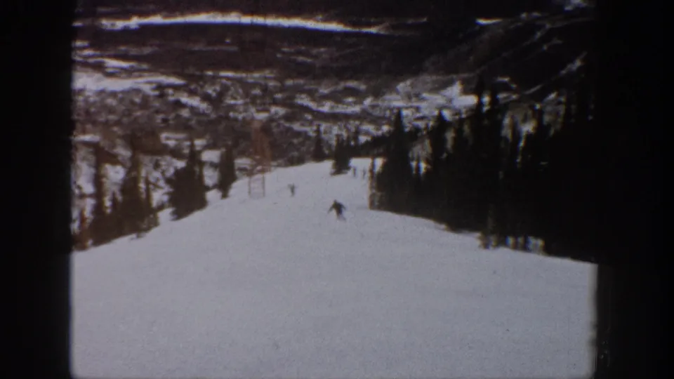 A dark-clad skier descends the lower part of the snowy Aspen run, seen through grainy 8mm home-movie framing.