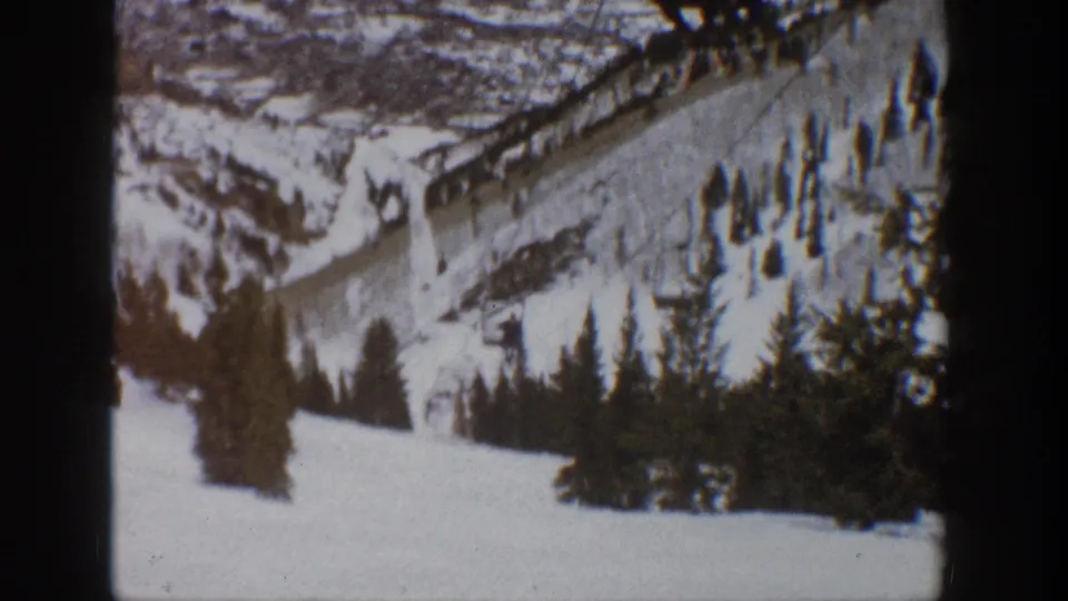 1961 Aspen frame looking down a snow-covered mountain run toward trees, valley terrain, and distant slopes.