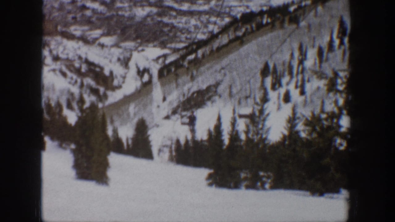 1961 Aspen home-movie frame showing a snowy ski slope, lift line, evergreen trees, and distant mountain ridges.