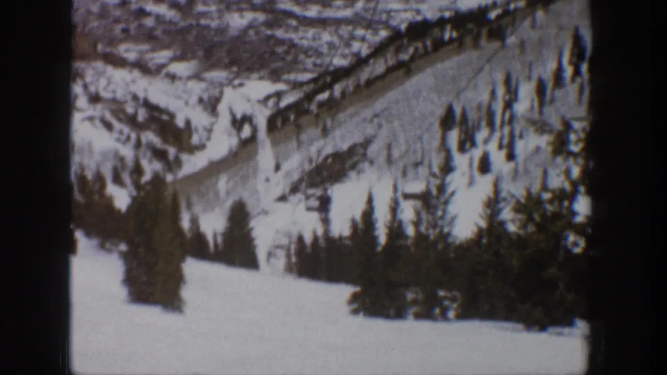 1961 Aspen home-movie frame showing a snowy ski slope, lift line, evergreen trees, and distant mountain ridges.