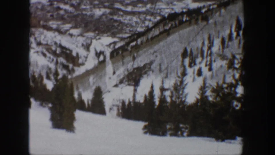 Vintage Aspen winter frame with a lift line ascending a snow-covered hillside above dark evergreen trees.
