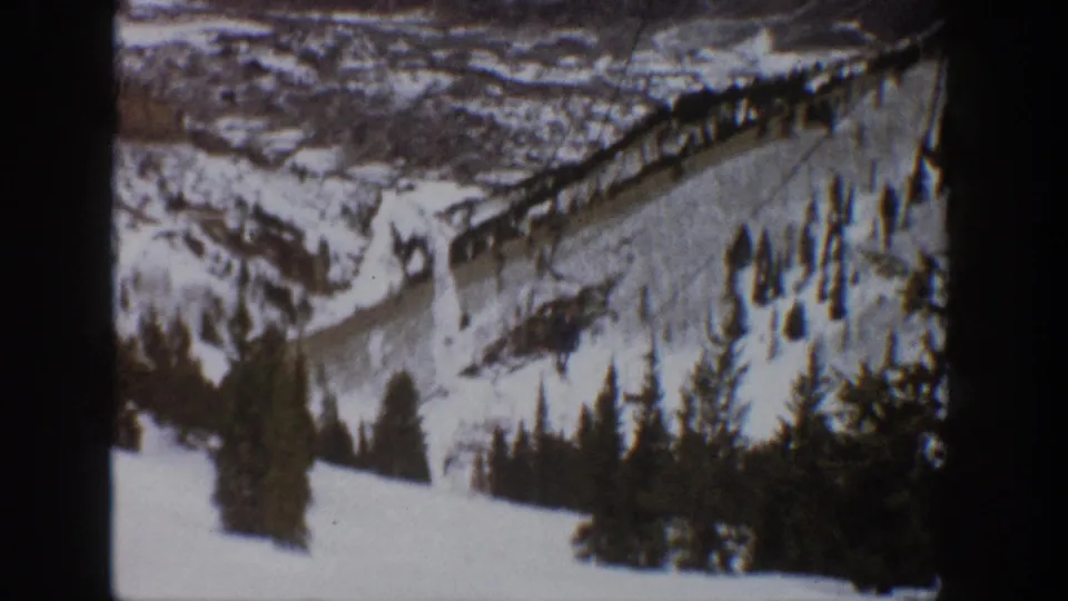 1961 home-movie view of an Aspen ski run with a lift line, trees, and dark gate borders from the 8mm scan.
