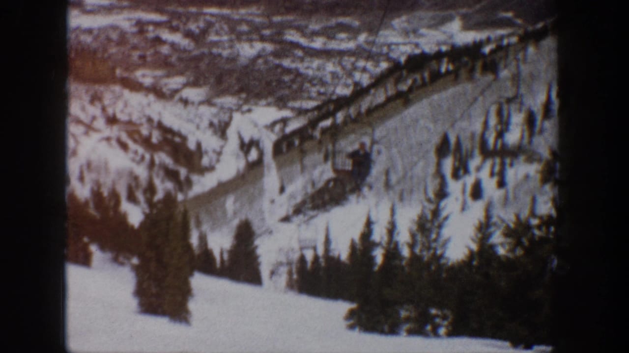 1961 Aspen, Colorado home-movie frame showing a snowy mountain ski slope with lift infrastructure, evergreen trees, and distant ridgelines.