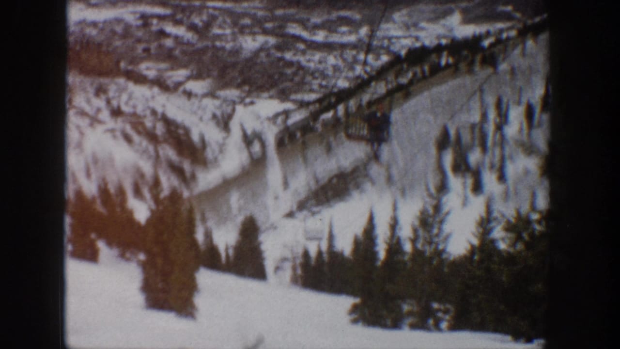 Snowy ski area with lift infrastructure, trees, and mountain terrain.
