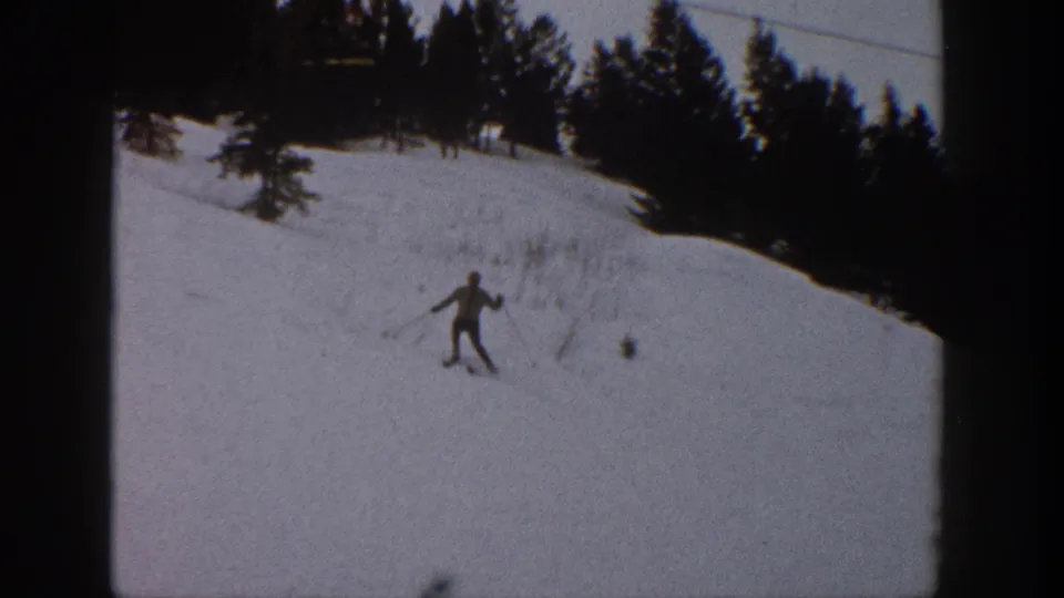 1961 Aspen, Colorado home-movie frame showing a distant skier crossing a snowy slope below dark evergreen trees.