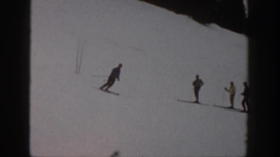 On a 1961 Aspen ski slope, one skier moves across open snow as a small group of skiers stands nearby watching or waiting.