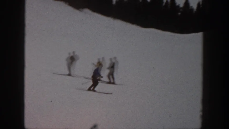 A foreground skier turns on the Aspen snow while several distant skiers stand together in the background, softened by motion blur and grain.