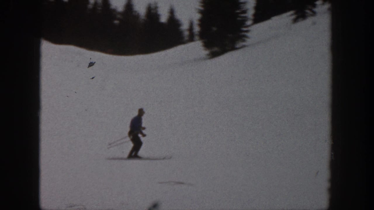 Adult skier descends a snowy Aspen slope in 1961 footage, with evergreen trees along the upper edge.