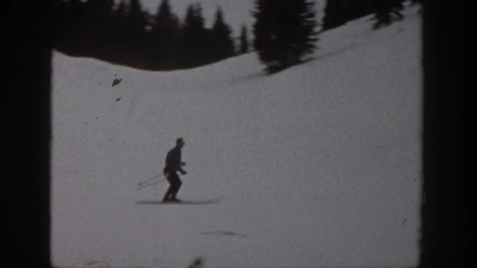 Adult skier descends a snowy Aspen slope in 1961 footage, with evergreen trees along the upper edge.
