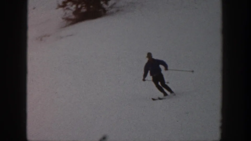 Adult skier continues downhill in 1961 Aspen home-movie footage, leaning through a turn on the snowy slope.