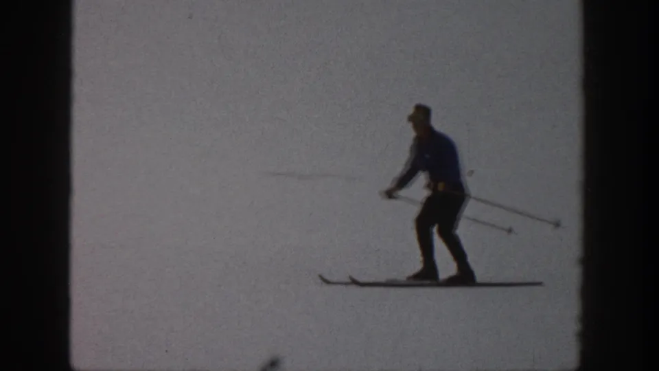 Adult skier crosses the frame on long skis in Aspen, Colorado, with sparse background detail in the snow.