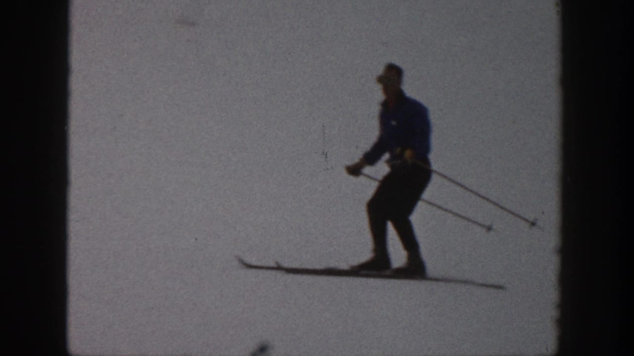 1961 Aspen home-movie frame of a skier in a blue jacket and dark pants moving across a high-contrast snow slope.