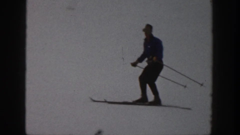 1961 Aspen home-movie frame of a skier in a blue jacket and dark pants moving across a high-contrast snow slope.