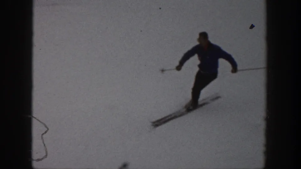 Aspen 1961 home-movie frame of a skier descending toward the camera, with poles spread and skis visible on the snow.
