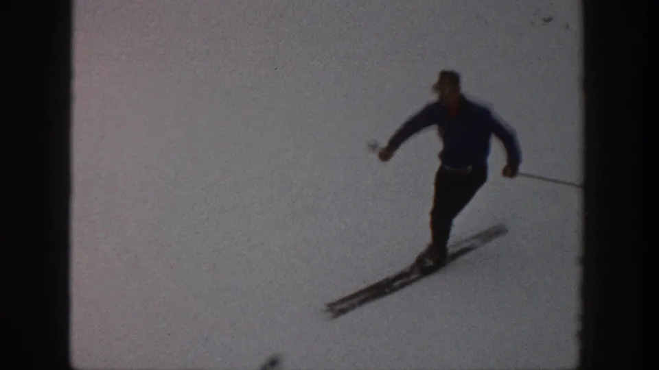 In 1961 Aspen home-movie footage, a man in a blue sweater and dark pants skis across a pale snowy slope.