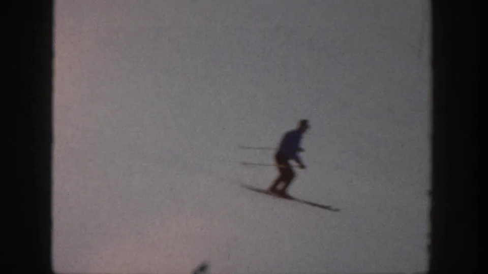 The skier appears small in the frame while gliding across an open snowy Aspen slope in vintage 8mm footage.