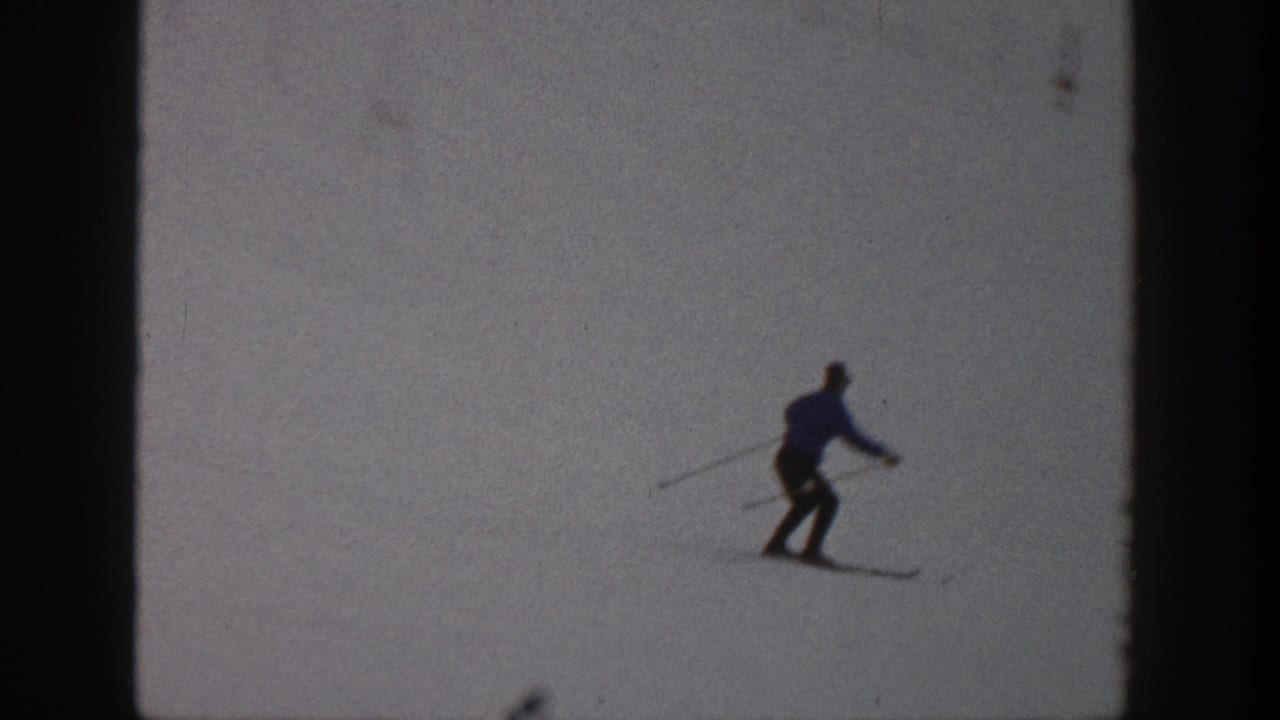 A distant skier in dark winter clothing moves across a snowy Aspen slope in 1961 home-movie footage.