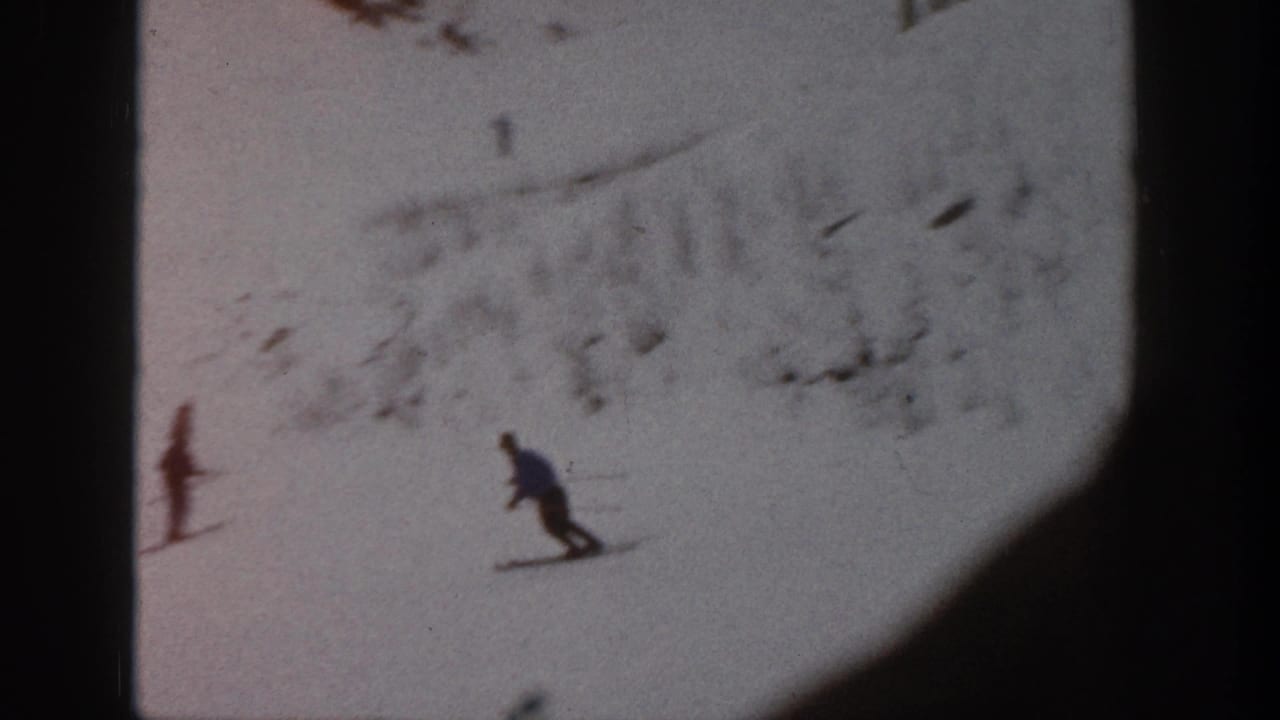 Two distant skiers descend a snowy slope near exposed rocky patches.