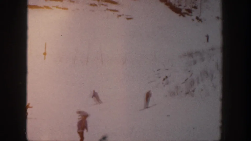 Distant skiers on a snowy Aspen slope appear through warm faded color and heavy 8mm home-movie grain.