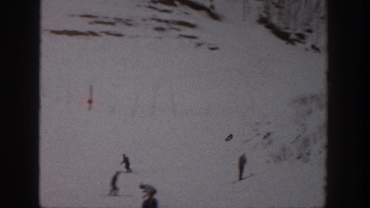 1961 Aspen home-movie frame showing small skiers crossing a snow-covered slope, with film grain, scratches, and dark frame edges.