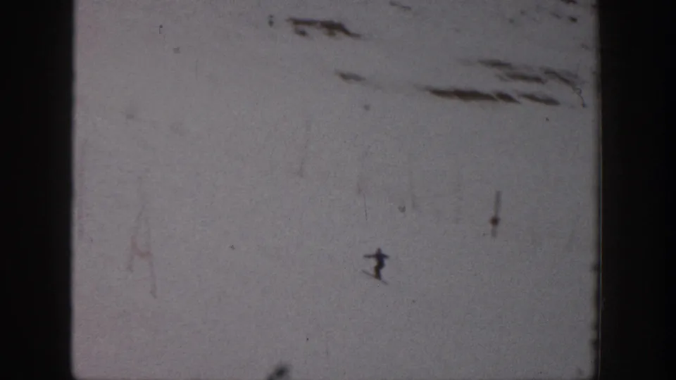 A distant skier moves downhill on the Aspen snowfield, framed by soft focus, grain, and vertical film-edge shadows.