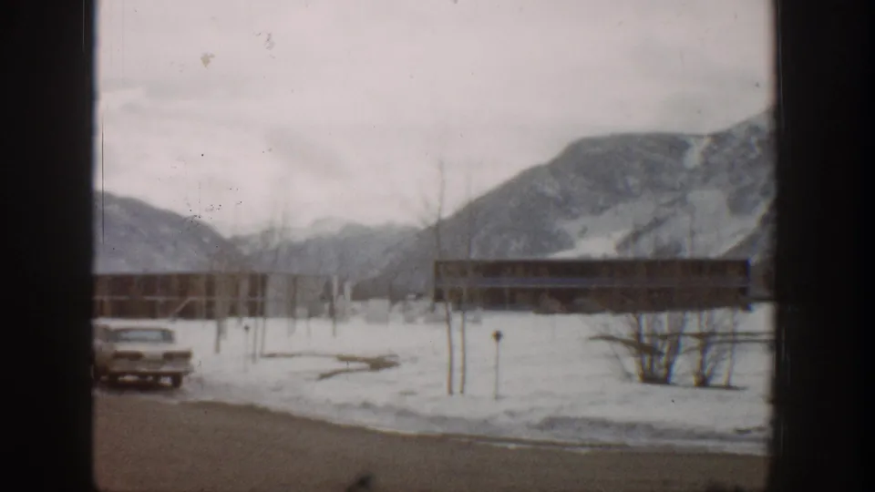A snowy Aspen roadside view shows a parked car, a long low building, bare trees, and mountain slopes.