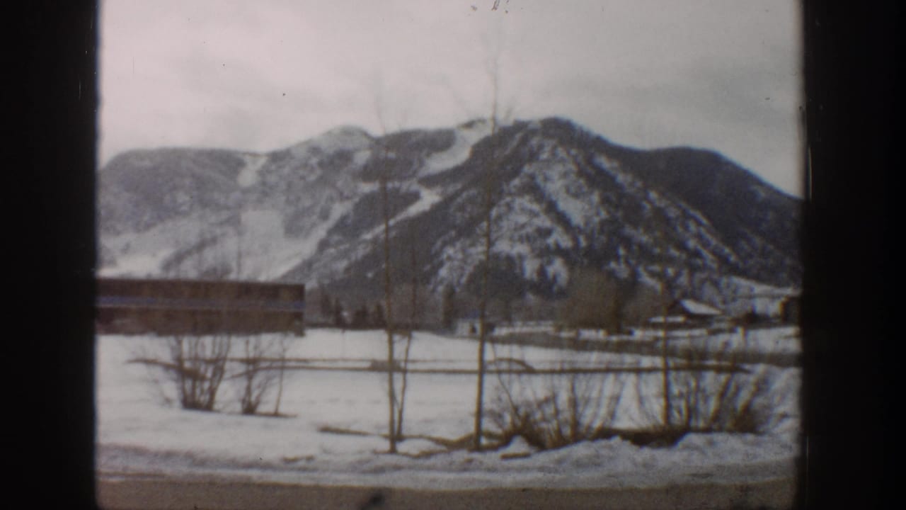 1961 Aspen, Colorado home-movie view of snow-covered ground, a low structure, leafless trees, and distant winter mountains.