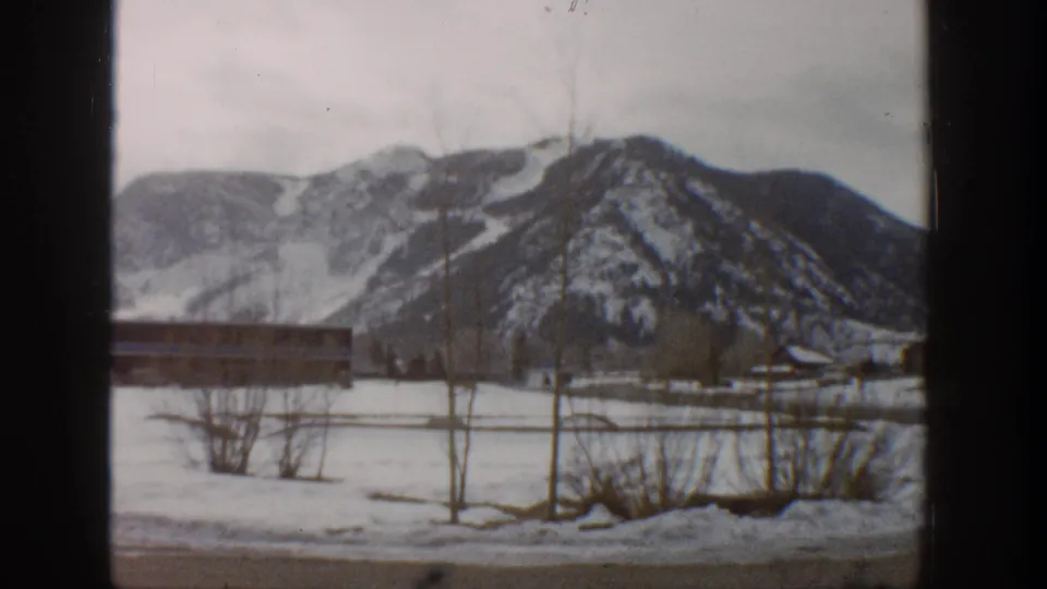 1961 Aspen, Colorado home-movie view of snow-covered ground, a low structure, leafless trees, and distant winter mountains.