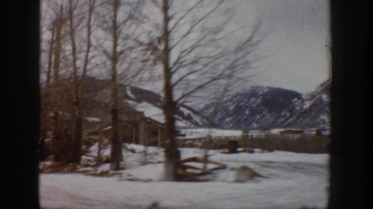 1961 Aspen, Colorado winter view across bare trees, split-rail fencing, snow, and dark mountain slopes.
