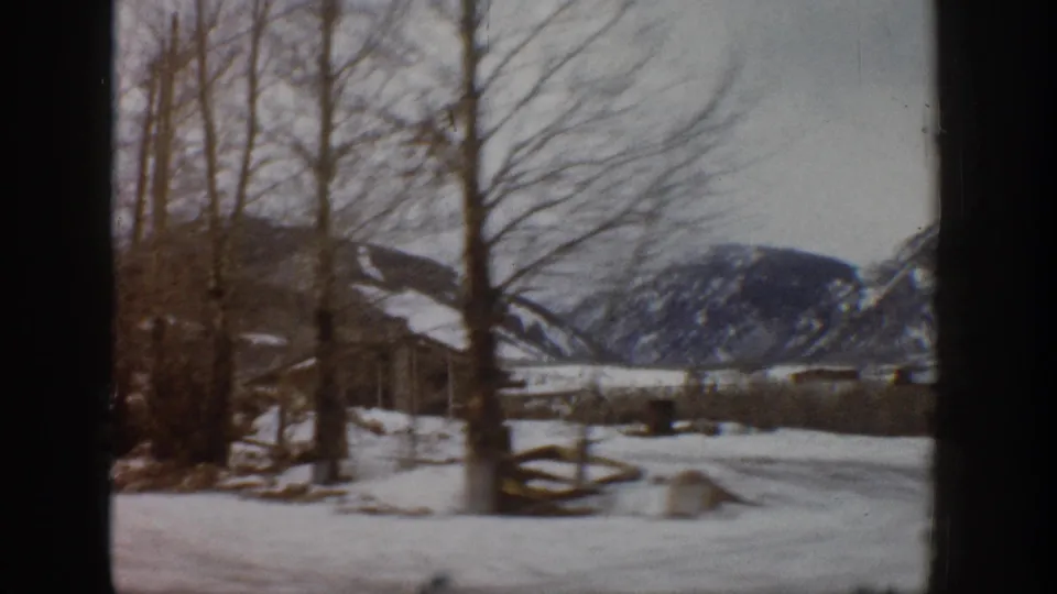 1961 Aspen, Colorado winter view across bare trees, split-rail fencing, snow, and dark mountain slopes.