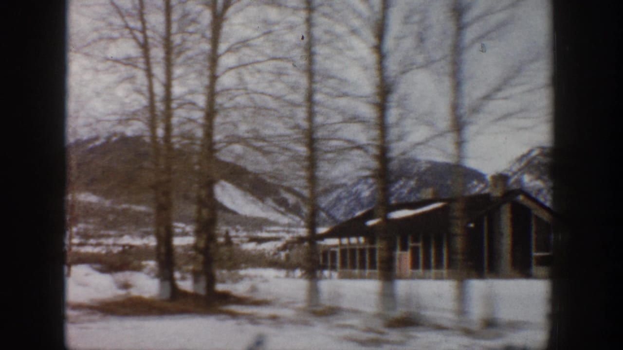 1961 Aspen, Colorado home-movie frame showing snow, leafless trees, mountain slopes, and a low lodge-like building.