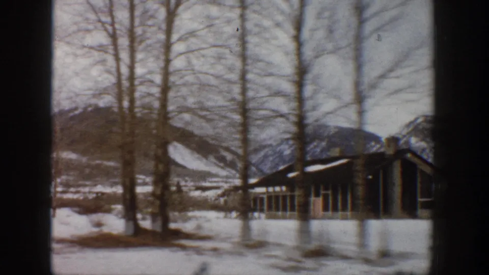1961 Aspen, Colorado home-movie frame showing snow, leafless trees, mountain slopes, and a low lodge-like building.