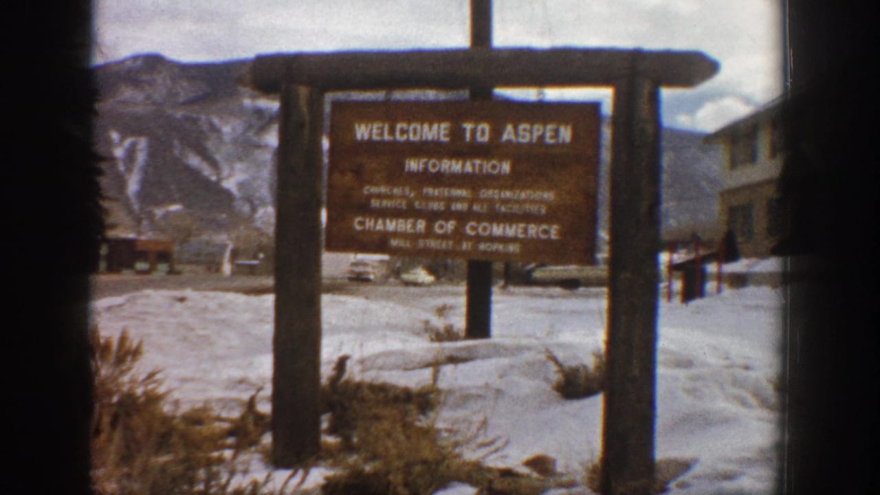 The Aspen visitor information sign remains centered in a snowy roadside view, with distant mountains and soft 8mm color visible in the frame.