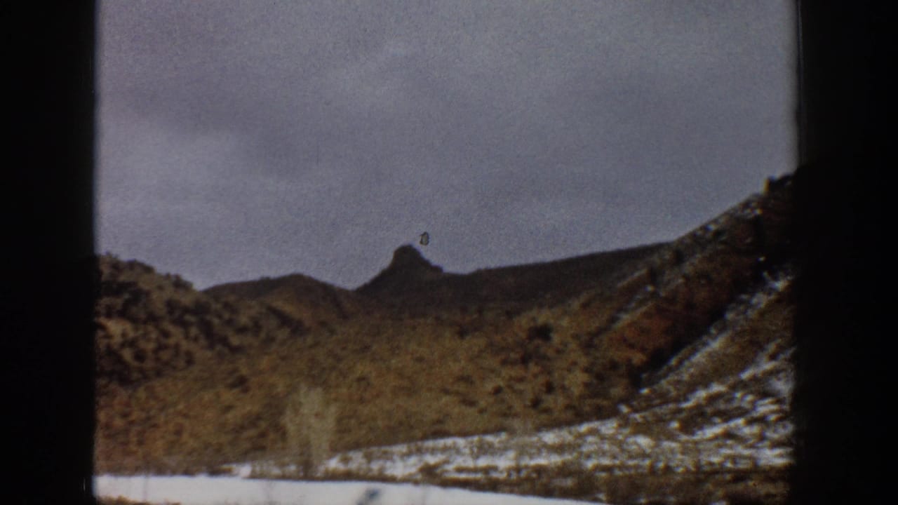 Snowy hillside and pointed mountain ridge viewed from a moving car.