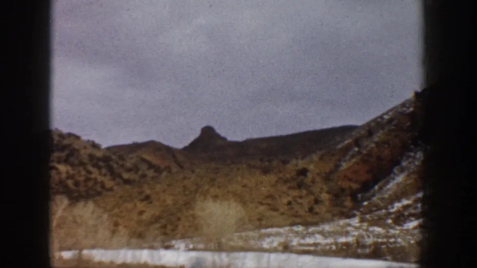 1961 Aspen-area 8mm frame of a brushy snow-patched valley and low mountain ridge, partially obscured by the contact-sheet frame divider.