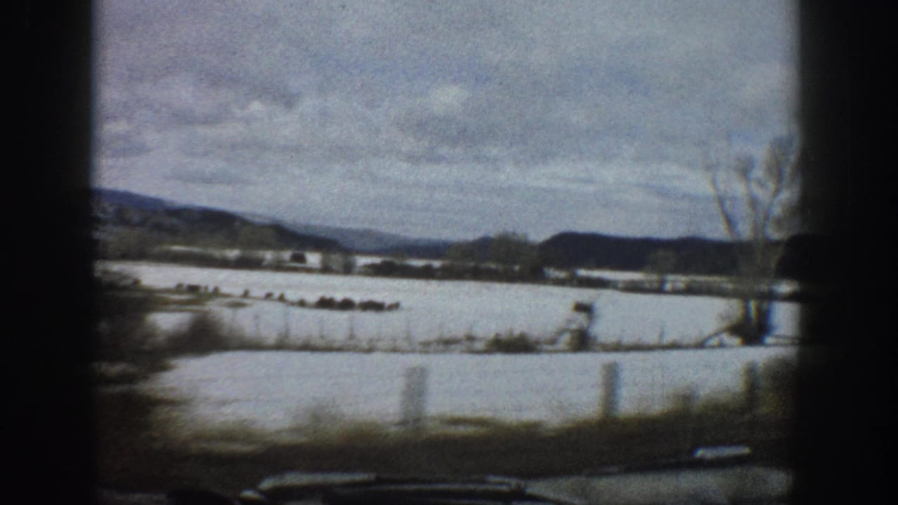 1961 Aspen, Colorado home-movie frame showing snowy fields, a wide river or floodplain, bare trees, and distant hills from a moving vehicle.