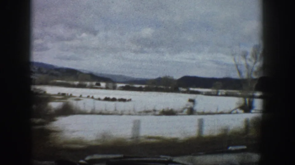 1961 Aspen, Colorado home-movie frame showing snowy fields, a wide river or floodplain, bare trees, and distant hills from a moving vehicle.