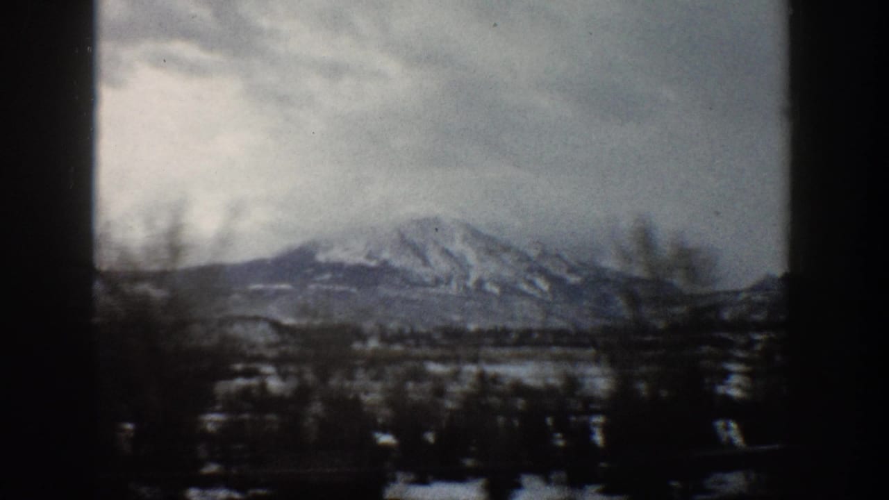 Aspen, Colorado 1961 8mm frame showing distant snow-capped mountains, dark foreground trees, and a cloudy winter sky.