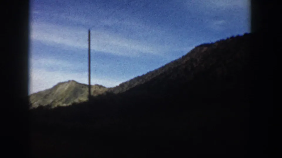 Final 8mm frame from the Aspen, Colorado clip showing a tall pole, blue sky, rocky hillside, and dark mountain slope.