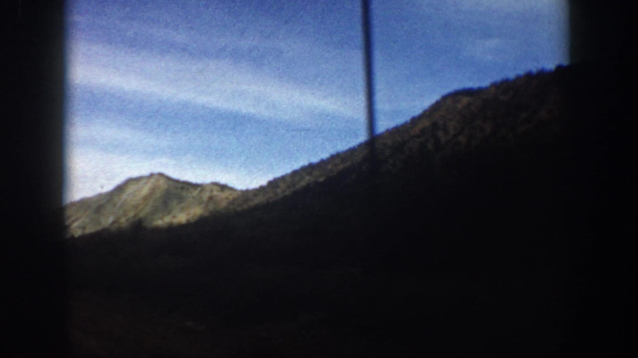 1961 Aspen-area 8mm frame showing a mountain valley viewed through dark window or film-edge framing, with a sunlit peak and blue sky.